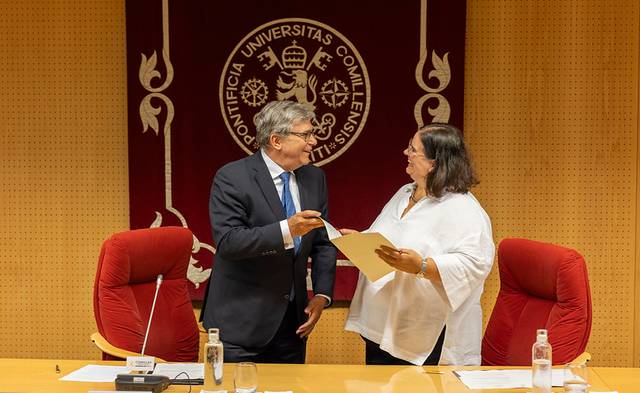 Dos personas intercambian documentos en un acto oficial en una universidad.