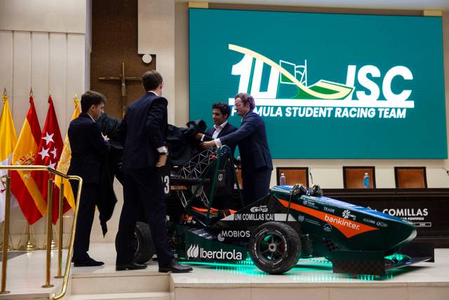 Un grupo de estudiantes presenta un prototipo de auto de carreras en un evento formal.