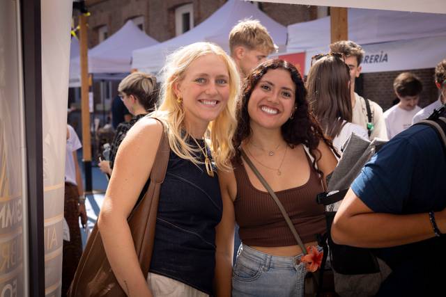 Dos amigas sonrientes posan juntas en un evento al aire libre.