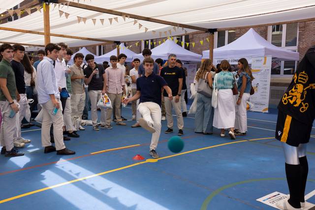 Un grupo de jóvenes observa a un chico mientras lanza una pelota en un evento al aire libre.