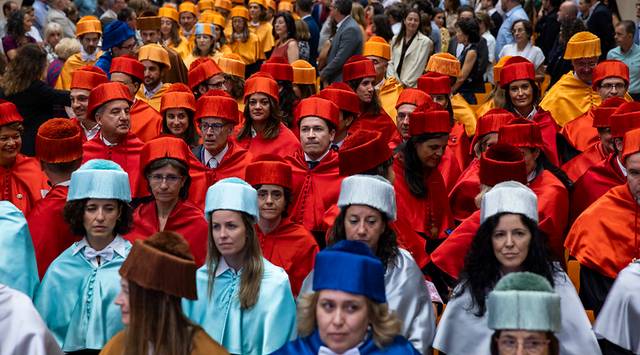 Un grupo de personas vestidas con capas y birretes de diferentes colores se encuentra agrupado en un evento formal.