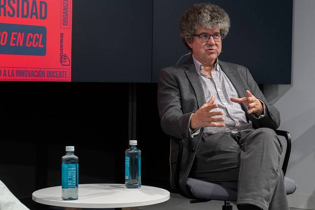 Un hombre con cabello rizado y gafas habla mientras gesticula en un evento sobre innovación educativa.