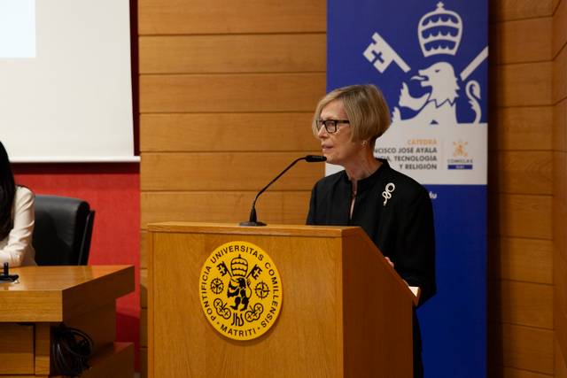Una mujer está hablando en un evento académico detrás de un podio con el logo de una universidad.