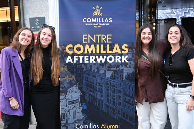 Un grupo de cuatro jóvenes posando frente a un cartel de un evento de la Universidad Pontificia Comillas.