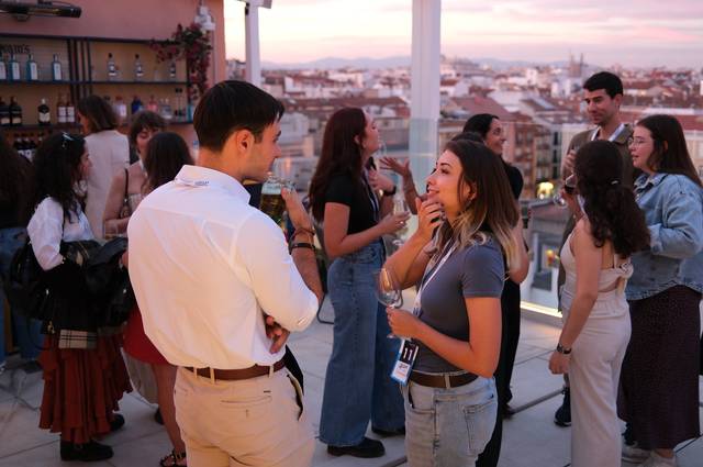 Un grupo de personas socializa en una terraza al atardecer con vistas a la ciudad.