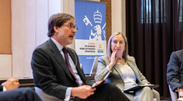 Un panel de discusión con dos personas hablando y un fondo institucional.