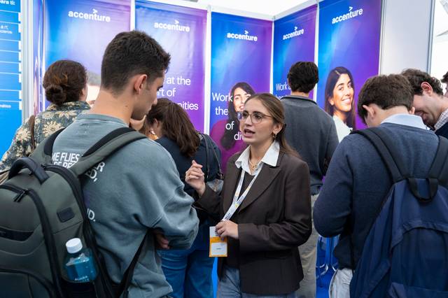 Una mujer habla con un grupo de personas en un evento de presentación de la empresa Accenture.