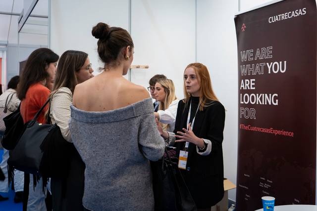 Un grupo de mujeres conversa en un evento profesional junto a un cartel de la empresa Cuatrecasas.