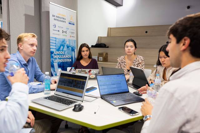 Un grupo de seis personas discutiendo en una reunión rodeados de computadoras portátiles y botellas de agua.