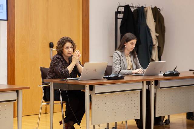 Dos mujeres participando en una reunión, una de ellas hablando y la otra trabajando en su computadora portátil.