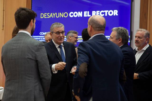 Un grupo de hombres conversan animadamente en un evento titulado 'Desayuno con el Rector'.