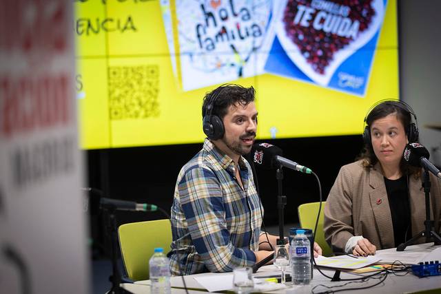 Dos personas participan en una transmisión en vivo de radio con fondo colorido.
