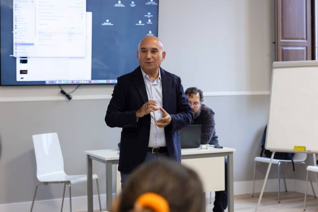 Un hombre de negocios está hablando en una sala de conferencias mientras otros escuchan atentamente.