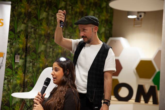 Una mujer está sentada frente a un hombre que sostiene un micrófono en una presentación.