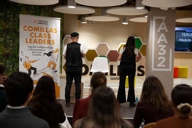 La imagen muestra un evento en una sala con un banner de Comillas Class Leaders y dos personas de espaldas frente a la audiencia.