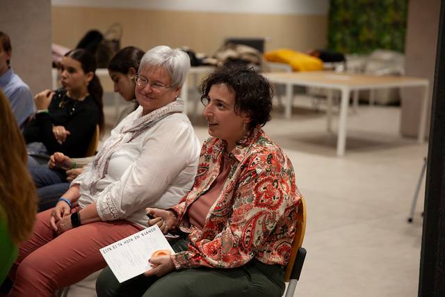 Un grupo de mujeres sentadas en un entorno social, algunas conversando y otras escuchando.
