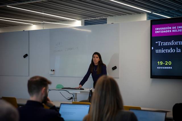 Una mujer está dando una presentación frente a un grupo de personas en un aula moderna.