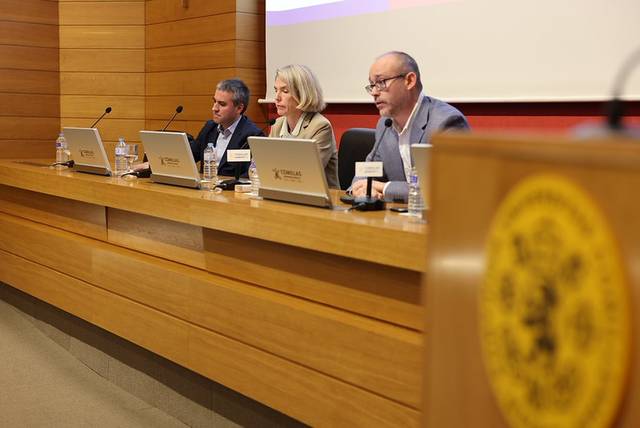 Tres personas sentadas detrás de un escritorio en un evento o conferencia.