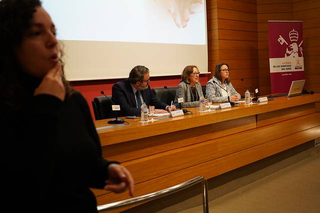 Una conferencia con varios oradores en un escenario y una intérprete en lengua de señas en primer plano.