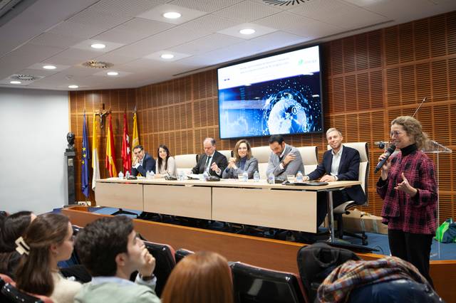 Una mujer está hablando frente a una audiencia en un evento que se lleva a cabo en una sala de conferencias.