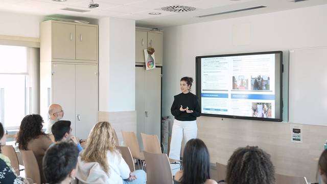 Una mujer está dando una presentación en una sala de clases frente a un grupo de personas.