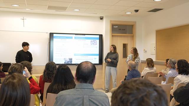 Un grupo de personas asiste a una presentación en un aula moderna, con un proyector mostrando información en la pantalla.