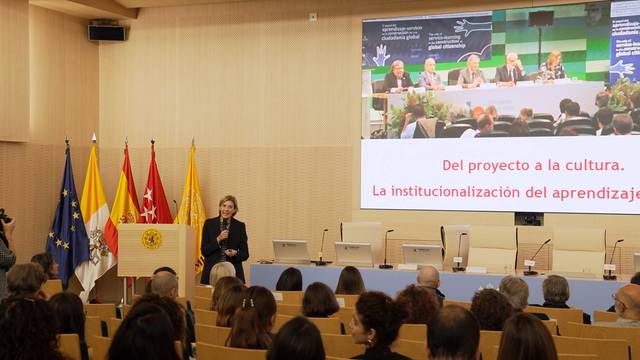 Una conferencista presenta un evento sobre la institucionalización del aprendizaje frente a un público atento.