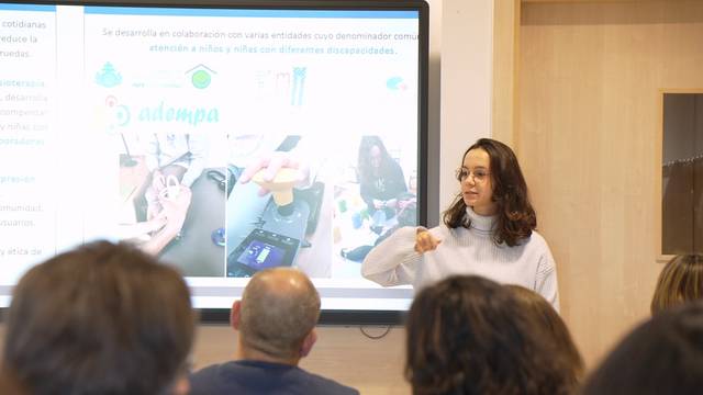 Una mujer está presentando un contenido en una proyección mientras un grupo de personas la observa.
