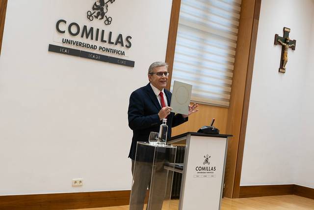 Un orador sostiene un libro mientras se presenta en un evento en la Universidad Pontificia Comillas.