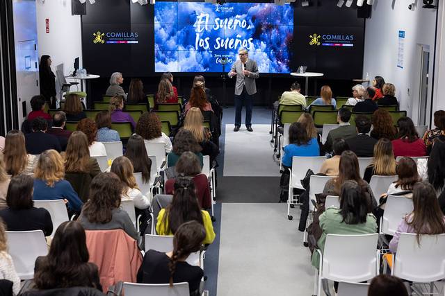 Un orador da una charla frente a un público atento en un auditorio moderno.