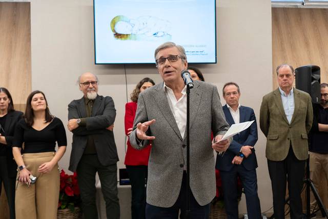 Un hombre habla frente a un público en un evento mientras se proyecta una imagen en una pantalla detrás de él.