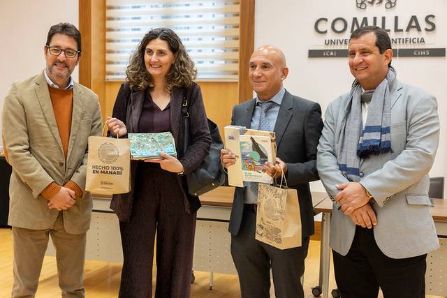 Cuatro personas posan sonrientes en un evento en la Universidad Comillas, sosteniendo varios objetos en sus manos.