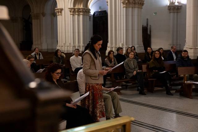 Una mujer lee en un acto dentro de una iglesia mientras el público la observa atentamente.