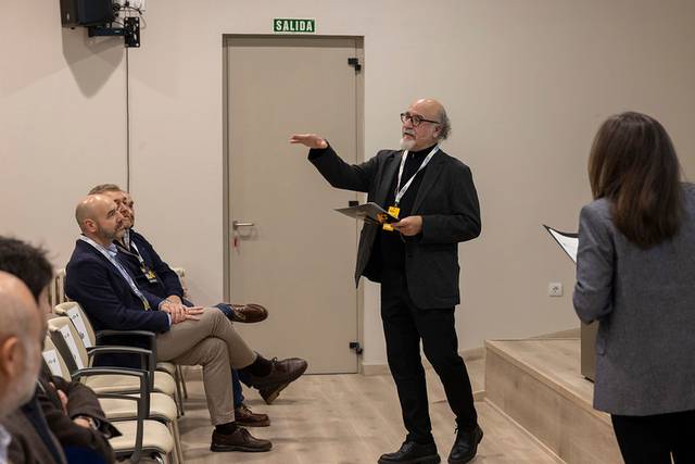 Un orador gesticula mientras presenta ante un público sentado en un auditorio.