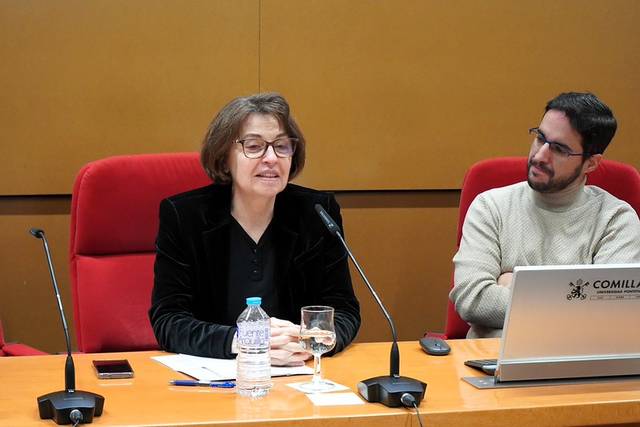 Mujer hablando en una conferencia mientras un hombre la escucha.