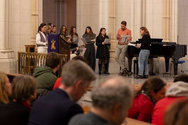 Un grupo de personas canta en un recinto con un piano y una atmósfera religiosa.