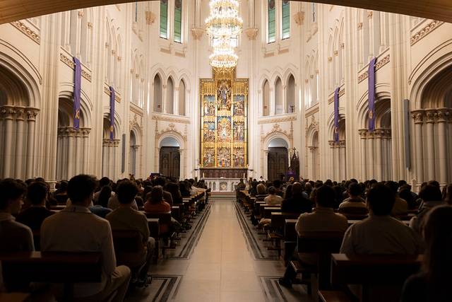 Un interior de iglesia con un gran altar iluminado y un público en asientos.