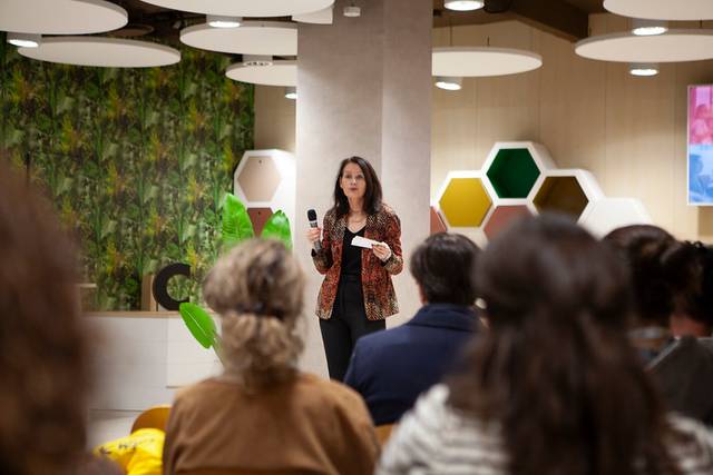 Una mujer está hablando en un evento mientras sostiene un micrófono frente a una audiencia.