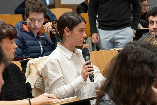 Una joven participa en una clase levantando la mano y sosteniendo un micrófono.