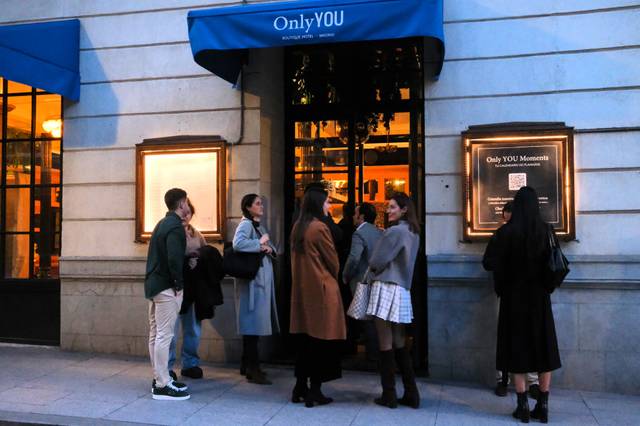 Un grupo de personas espera en la entrada de un establecimiento llamado Only YOU durante la tarde.