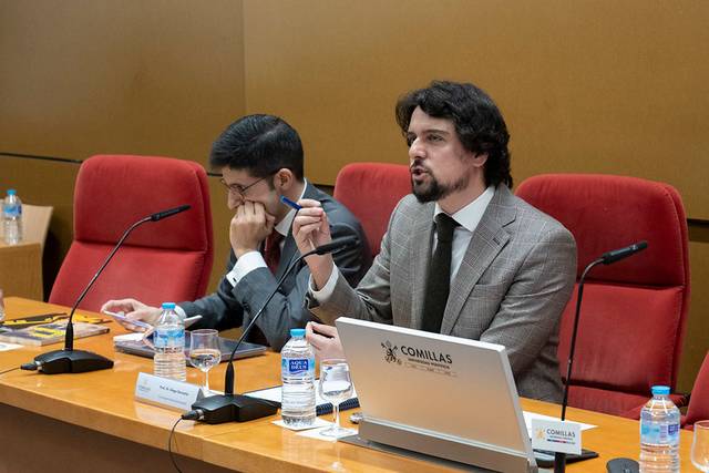 Un hombre habla en una mesa de conferencias mientras otro escucha atentamente.