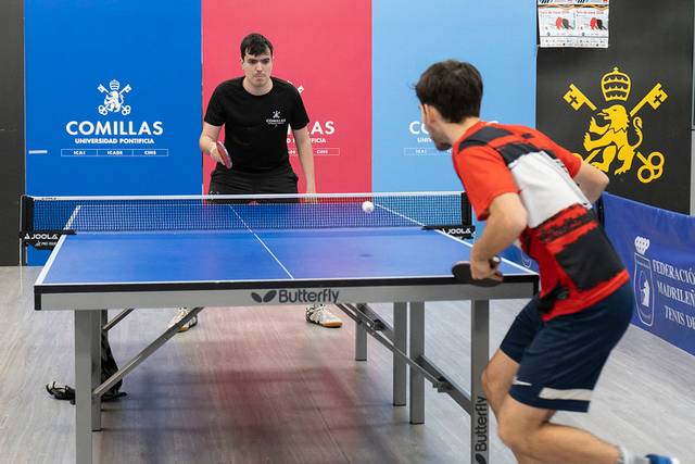 Dos jugadores compiten en una mesa de tenis de mesa, uno está preparado para recibir el golpe de la pelota.