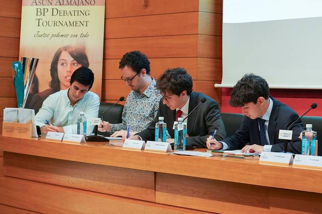 Cuatro jóvenes participan en un torneo de debate, concentrados y escribiendo sus notas.