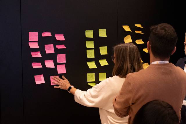 Un grupo de personas interactúa con notas adhesivas de colores en una pared negra.
