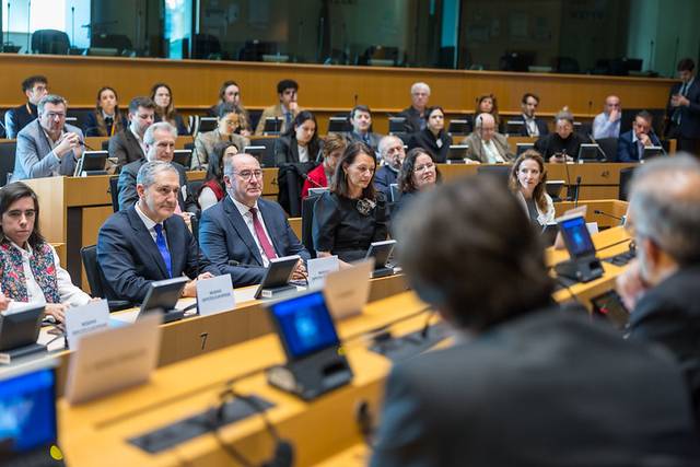 Una reunión con múltiples participantes sentados en un ambiente formal.