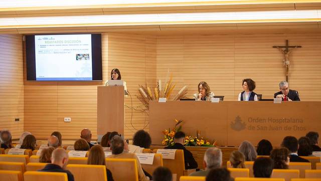 Una conferencia en un salón con varias personas escuchando a una ponente en el estrado.