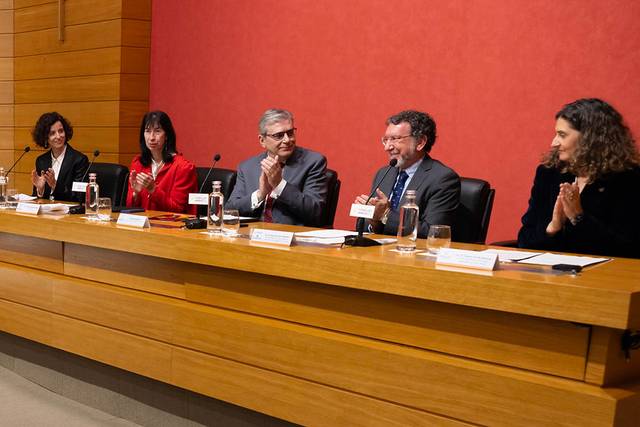 Un grupo de cinco personas sentadas en una mesa aplaudiendo en un evento formal.