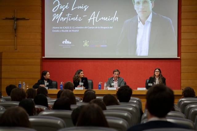 Un panel de discusión con varios ponentes frente a una audiencia en un salón con una proyección detrás.