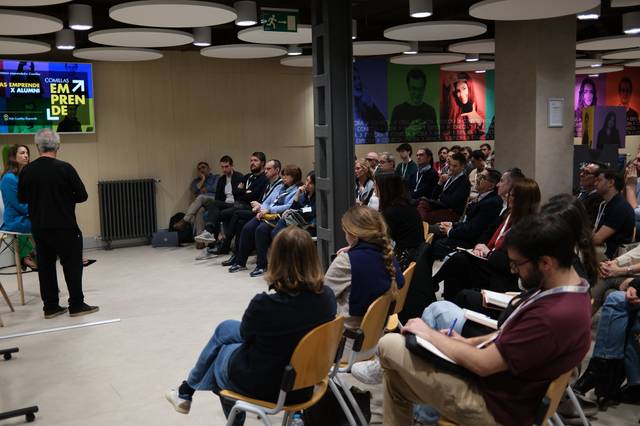 Una conferencia en la que un ponente habla frente a una audiencia en un espacio moderno.