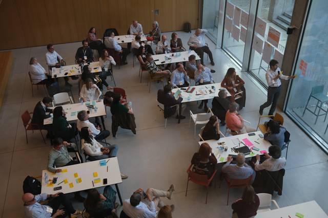 Una reunión grupal en un espacio moderno con varias personas sentadas alrededor de mesas.
